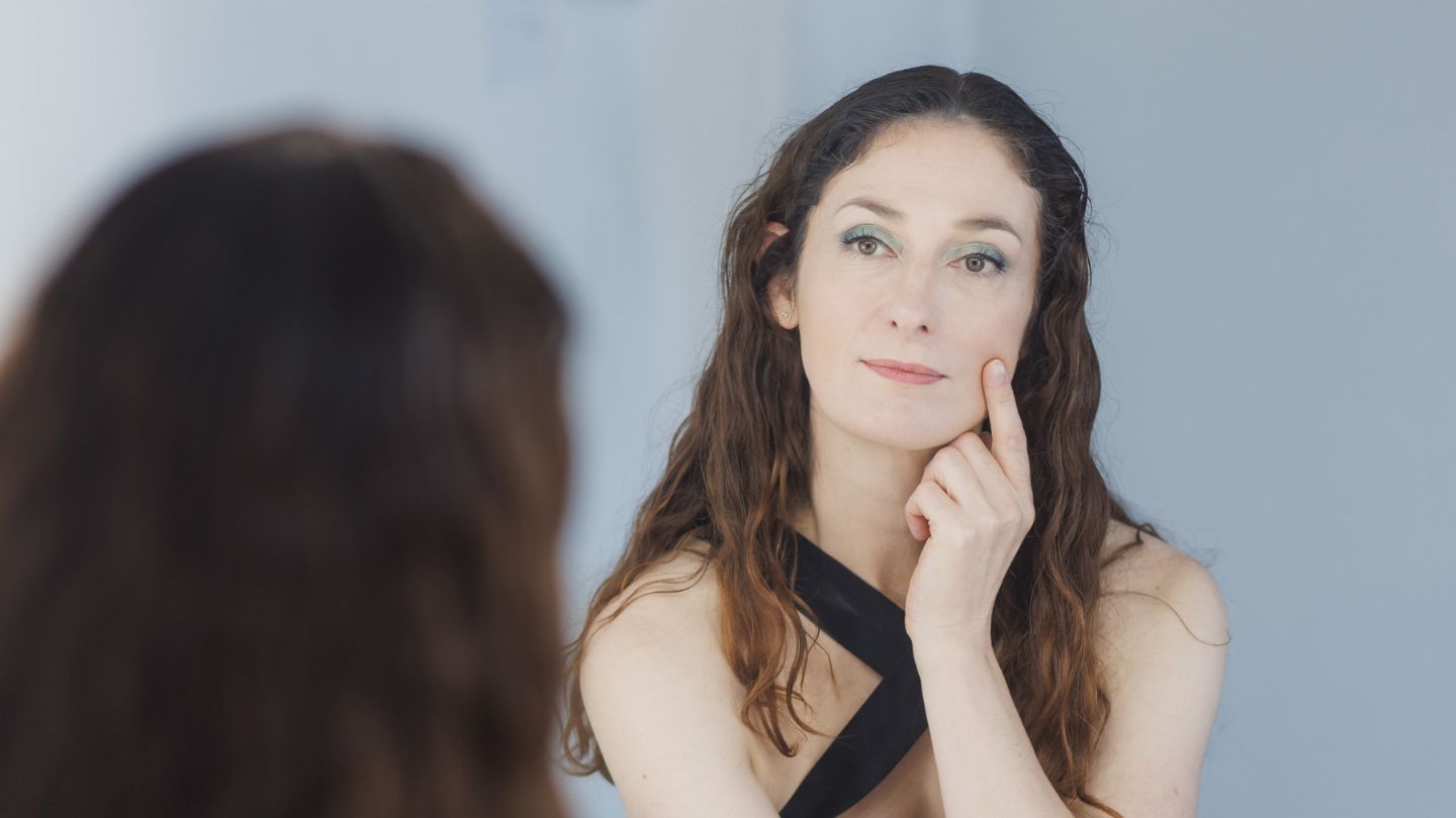 Woman over 40 looking in mirror and touching her face with Bonjou Beauty balm for soft, healthy mature skin skincare routine