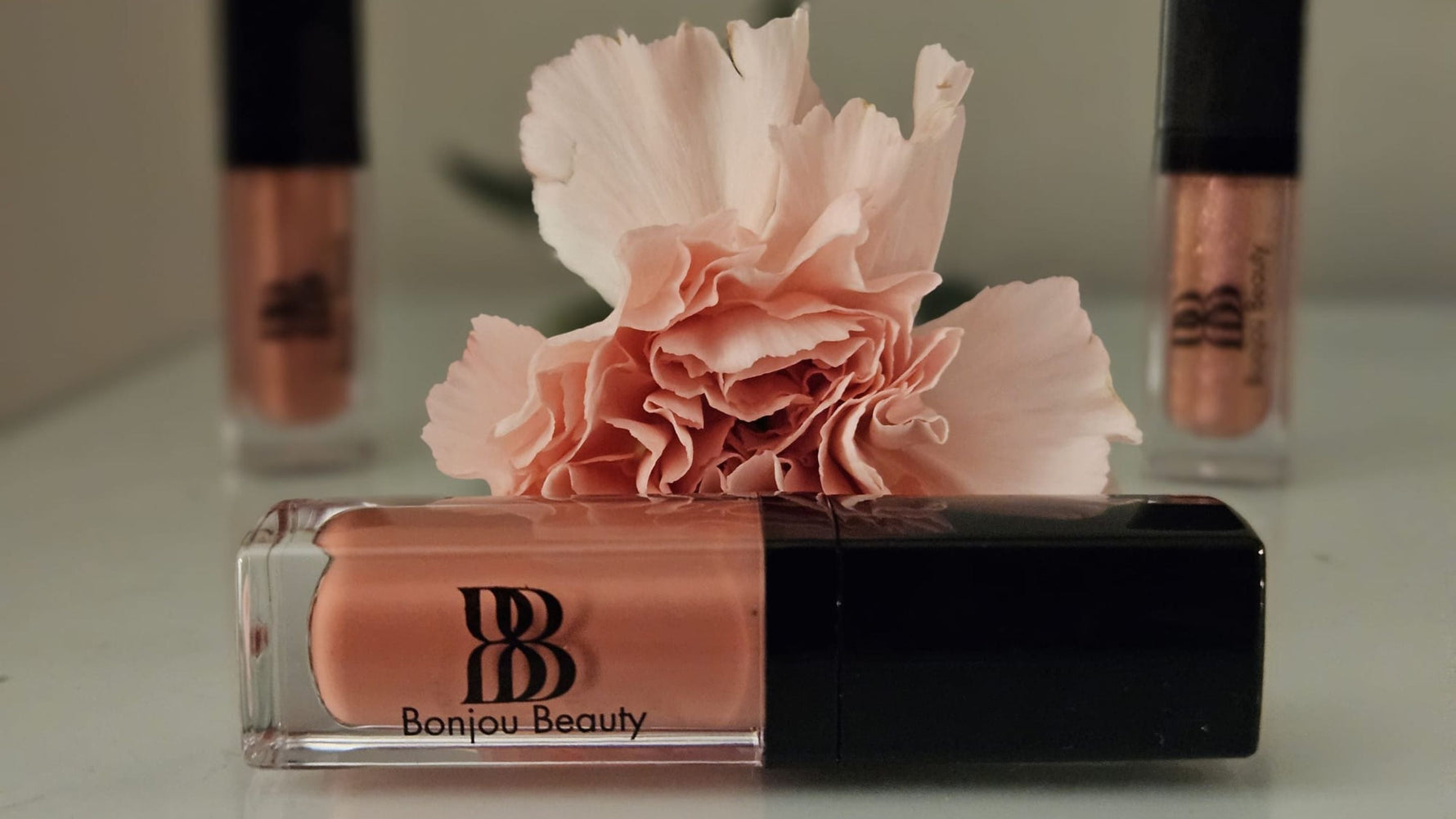 Bonjou Beauty pink lip gloss with flower on a grey (gray) table