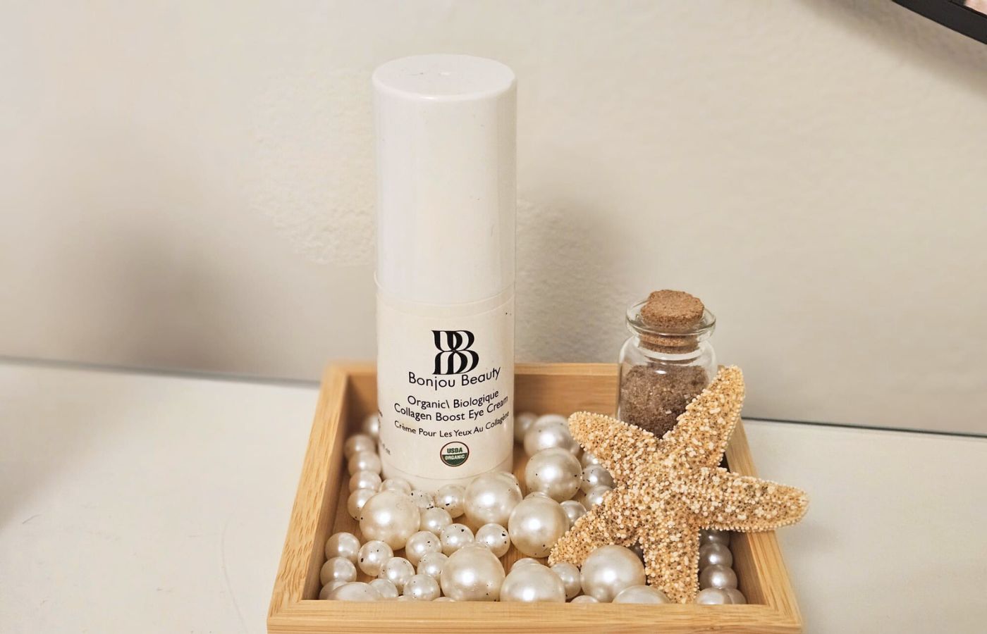 Bonjou Beauty eye cream in a box with faux pearls, a seasshell and bottle on a white table and background