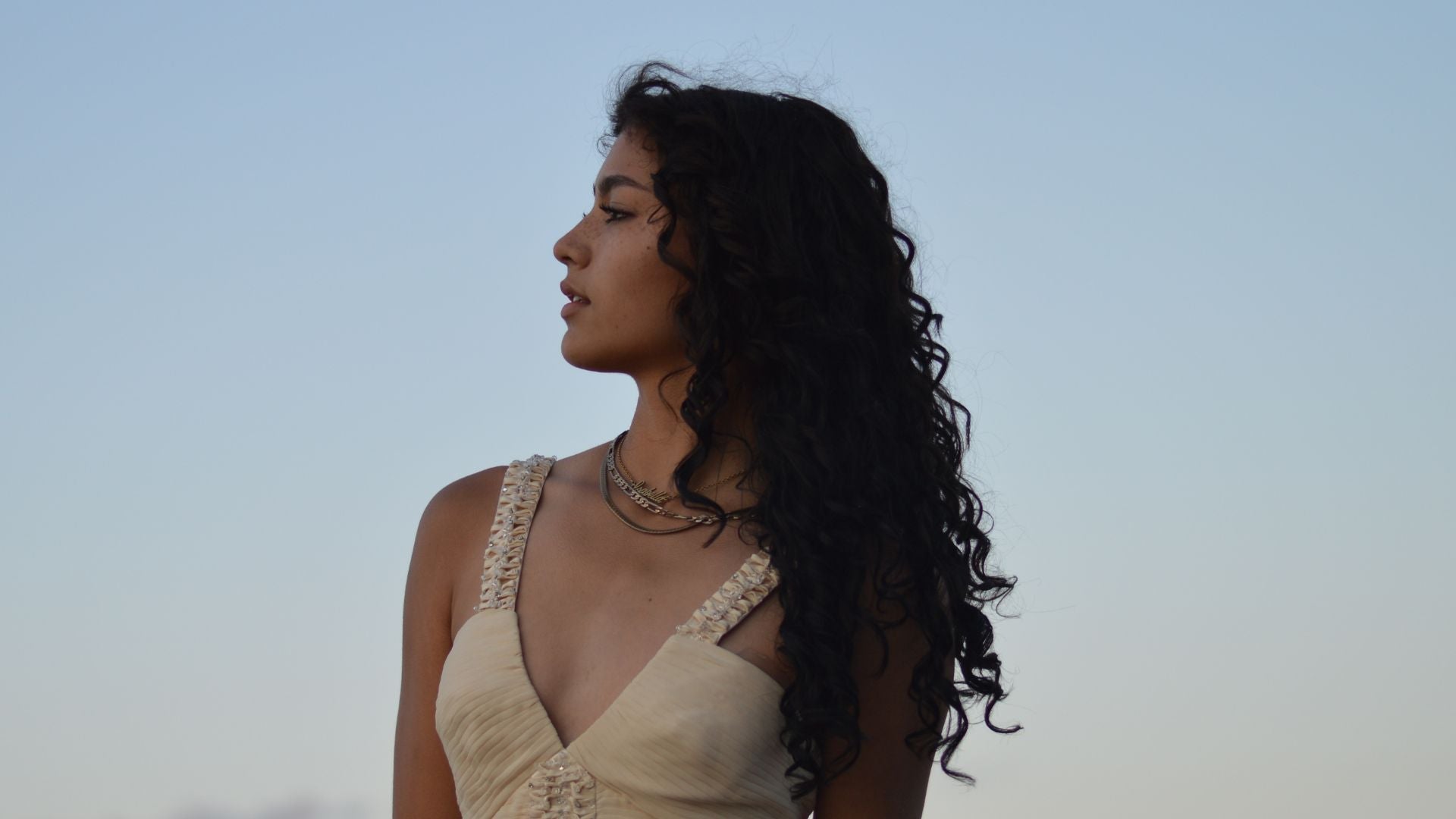 woman with curly dark hair in a white top with the sky as a background