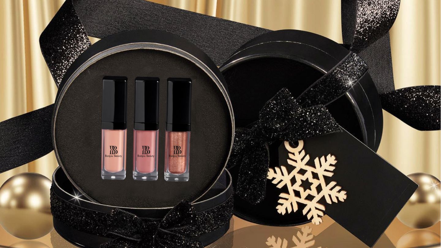 Three lip gloss shades in an open black gift box with bows and gold decorations