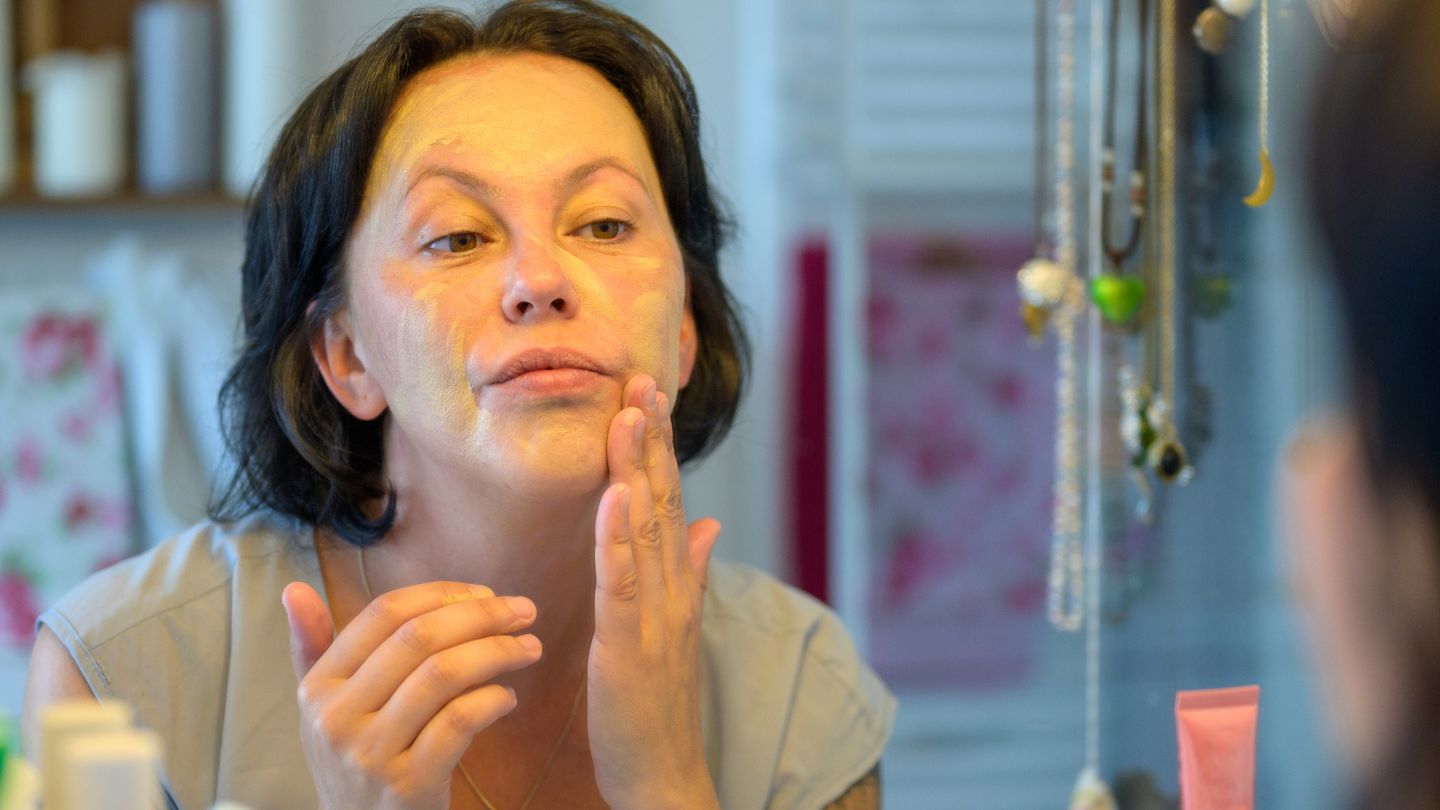 mature woman applying skincare mask to face in a mirror