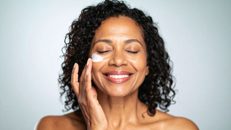 Woman applying cream to her face against a light gray background