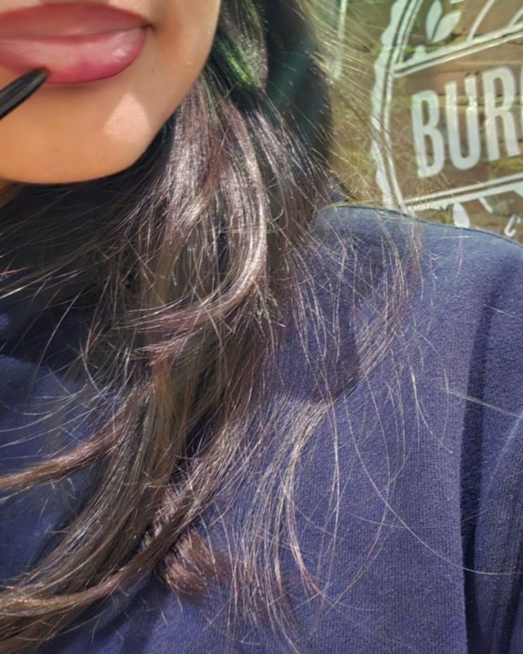 Close-up of my niece applying Bonjou Beauty lip liner with dark brown hair and a navy blue top against a blurred outdoor background.