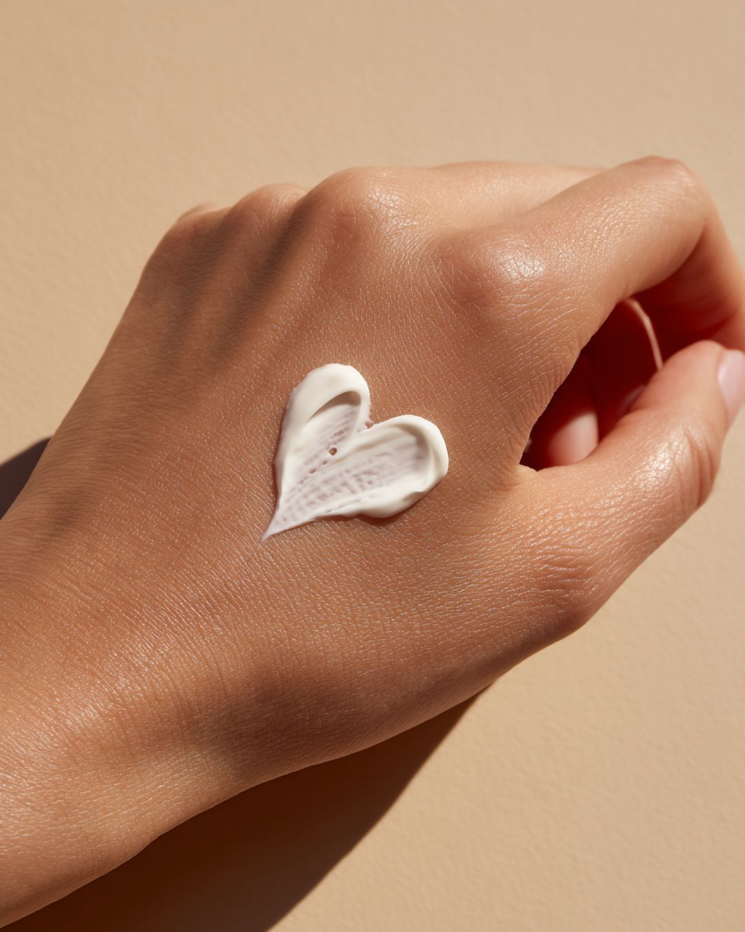 Hand with heart-shaped sunscreen on it on a beige background