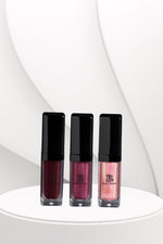 Three lip gloss bottles with black caps on a white platform