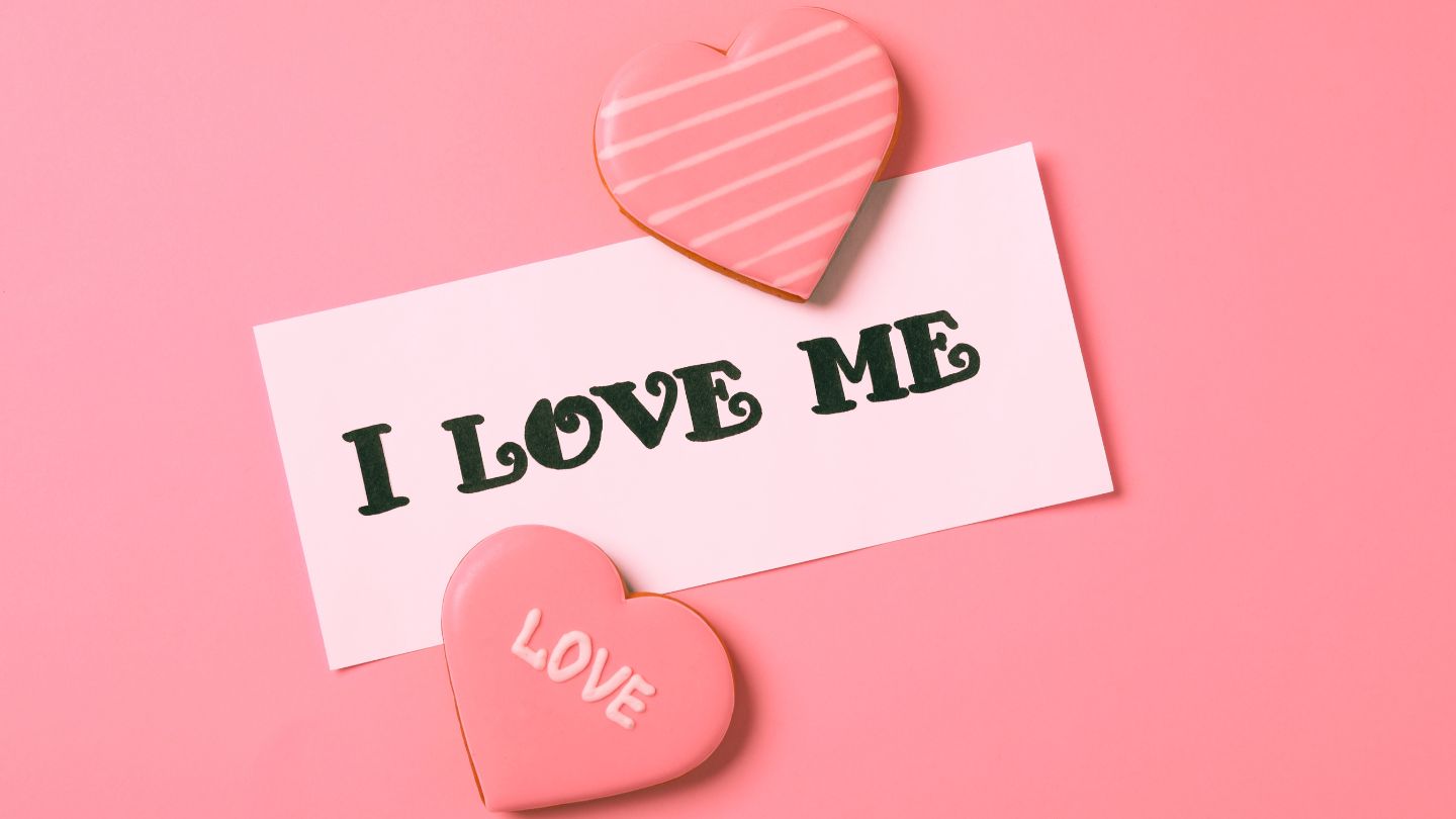 Note with 'I LOVE ME' text and heart-shaped cookies on a pink background